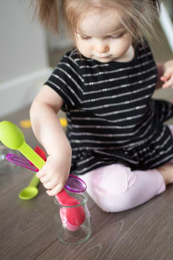 child putting colorful spoons in a jar