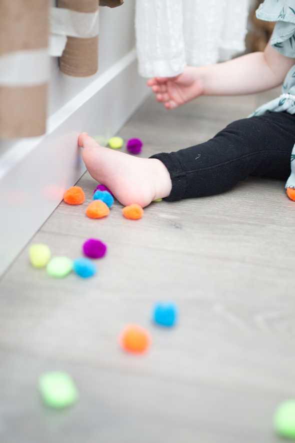 child's foot by pom poms and cardboard tubes taped to the wall