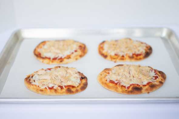 four pieces of naan bread topped with sauce, cheese, and chicken on a baking sheet