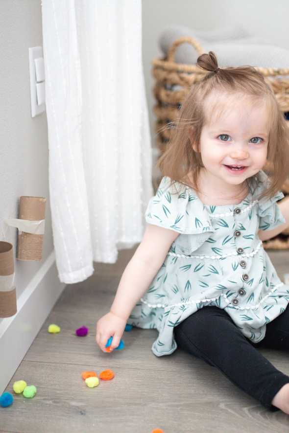 smiling child sitting by pom poms and tubes taped to the wall