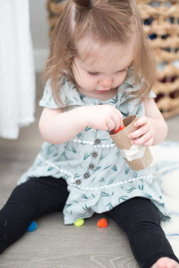 child dropping pom poms through tube being held in their hands