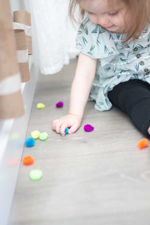 child sitting by pom poms and cardboard tubes taped to the wall