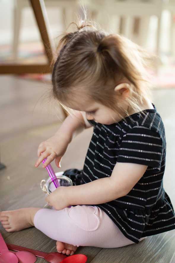 child putting colorful spoons in a jar